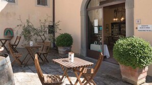 An outdoor seating area with wooden tables and chairs, potted plants, and a storefront with a sign. - Villa in Tuscany With Pool and Wine Tasting (Pergine Valdarno)