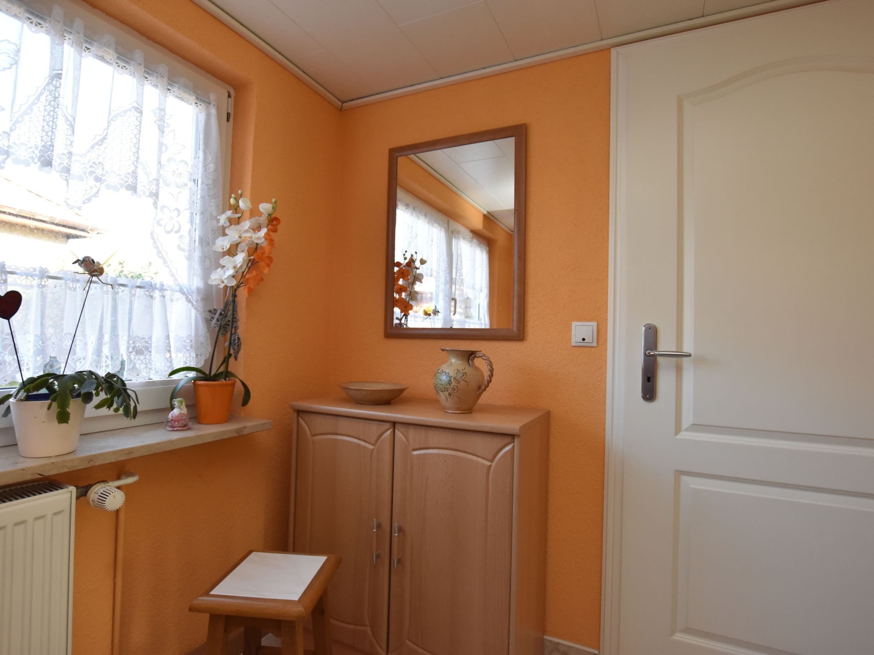 Una habitación con ventana, espejo, armario y una pequeña mesa.