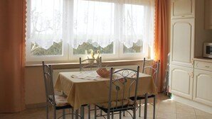 A dining area with a table set for four, a window with curtains, and a kitchen area with cabinets and a microwave. - Rustic Escape in Kropelin (Kroepelin)