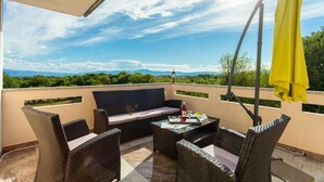 A terrace with wicker furniture, a table with a bottle and glasses, and a yellow umbrella. - Spacious Apartment in The Croatian Islands (Malinska-Dubasnica)