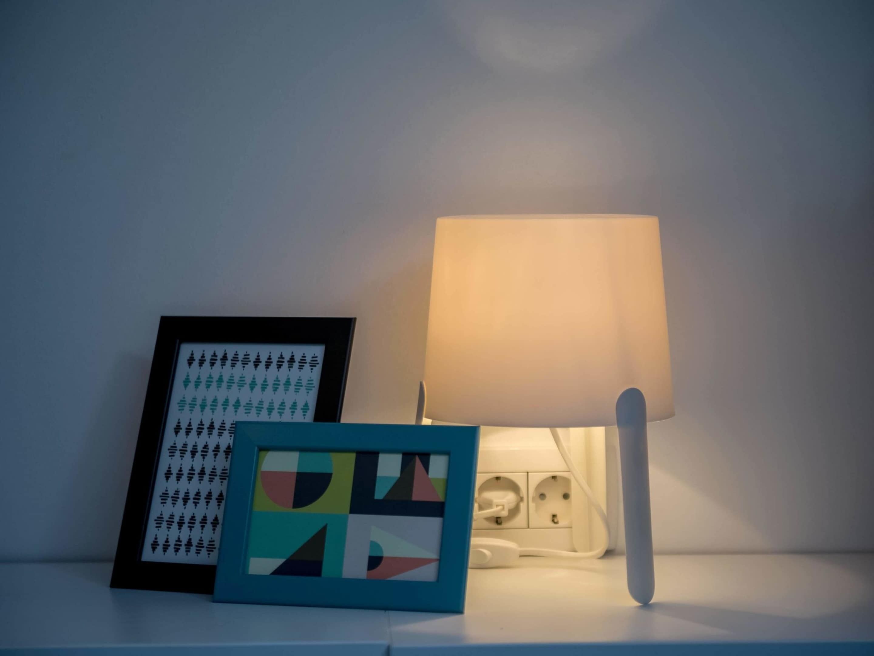Una mesita de noche con una lámpara y dos obras de arte enmarcadas.