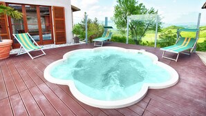 Een hottub op een houten terras met twee ligstoelen, een potplant en uitzicht op een groen landschap.