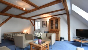 Een ruime loft met zichtbare houten balken, een gezellige zithoek met banken en een salontafel, een televisie en een kast met glazen deuren.