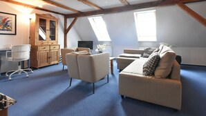 Ruime loft slaapkamer met zichtbare houten balken, een groot raam, een bureau en een comfortabele zithoek.
