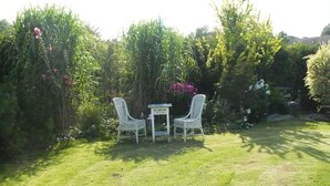 A garden with two white wicker chairs and a small table, surrounded by lush greenery and flowering plants. - Gemutliche Ferienwohnung mit Garten in Walkendorf (Walkendorf)