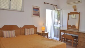 A bedroom with a large bed, a wooden dresser, a mirror, a nightstand with a lamp, and a door leading to a balcony. - Horacio Villa is Located near Center of Vilamoura (Loulé)