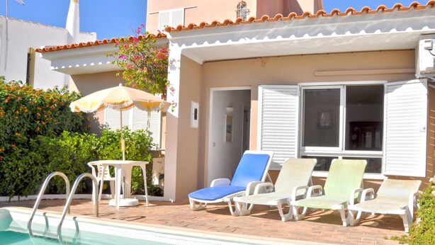 A poolside area with lounge chairs, a table, and an umbrella. - Horacio Villa is Located near Center of Vilamoura (Loulé)