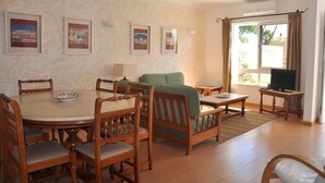 A dining area with a round table and chairs, a sofa, a television, and framed pictures on the wall. - Horacio Villa is Located near Center of Vilamoura (Loulé)