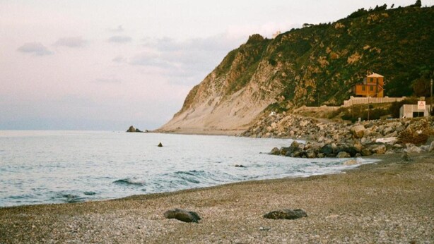 A coastal scene with a pebble beach, a rocky cliff, and a small building on the hillside. - Rustic Villa With Pool, Sicily (Castellammare del Golfo)
