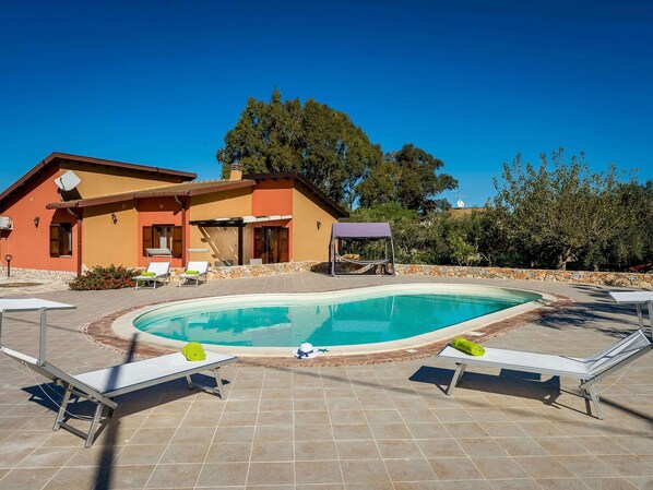 A pool area with lounge chairs, a covered seating area, and a stone wall. - Rustic Villa With Pool, Sicily (Castellammare del Golfo)