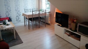 Ruokailutila, jossa on neljälle katettu ruokapöytä, jalustalla oleva televisio ja patteri.