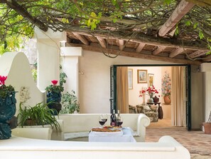 Un área de estar al aire libre con una mesa dispuesta para dos personas, una pérgola de madera sobre la cabeza y vistas a una habitación con un sofá y cortinas.