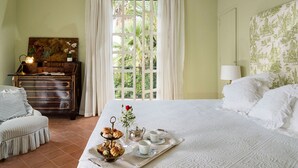 Un dormitorio con una cama, una mesita de noche con lámpara, una ventana con cortinas, un escritorio con lámpara y un cuadro en la pared.