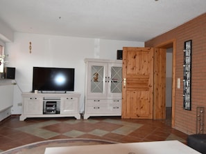 Ein Wohnzimmer mit einem Flachbildfernseher auf einem Schrank, einer Holztür und einem Fliesenboden.
