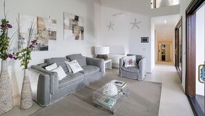 A modern living room with a grey sofa, a coffee table, and decorative items. There are abstract paintings on the wall and a starfish decoration. - Elegant House in Cefalù, Near the Sea With Stunning Views and Garden! (Cefalù)