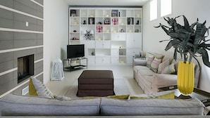 A modern living room with a grey sofa, a television, a bookshelf, and a large plant. - Elegant House in Cefalù, Near the Sea With Stunning Views and Garden! (Cefalù)