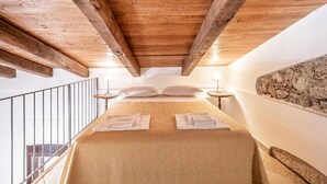 A bedroom with a wooden ceiling, a bed with white linens, two bedside tables with lamps, and a stone wall. - Holiday Home in Guardavalle by River (Stilo)