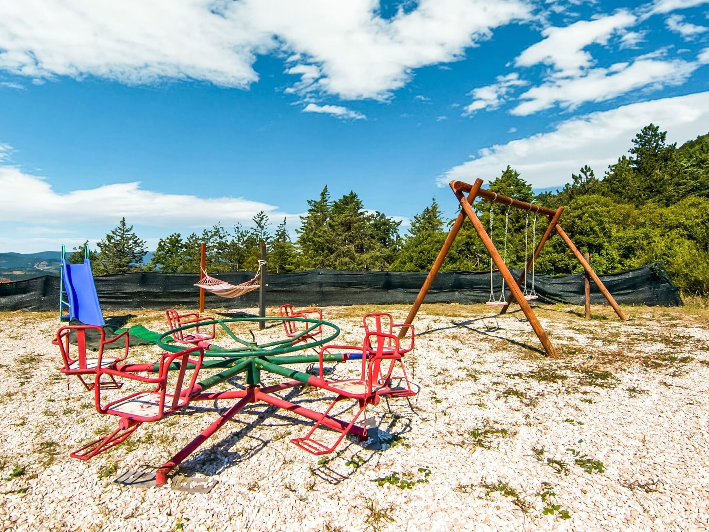 A playground with a swing set and a slide, surrounded by trees and a clear sky.