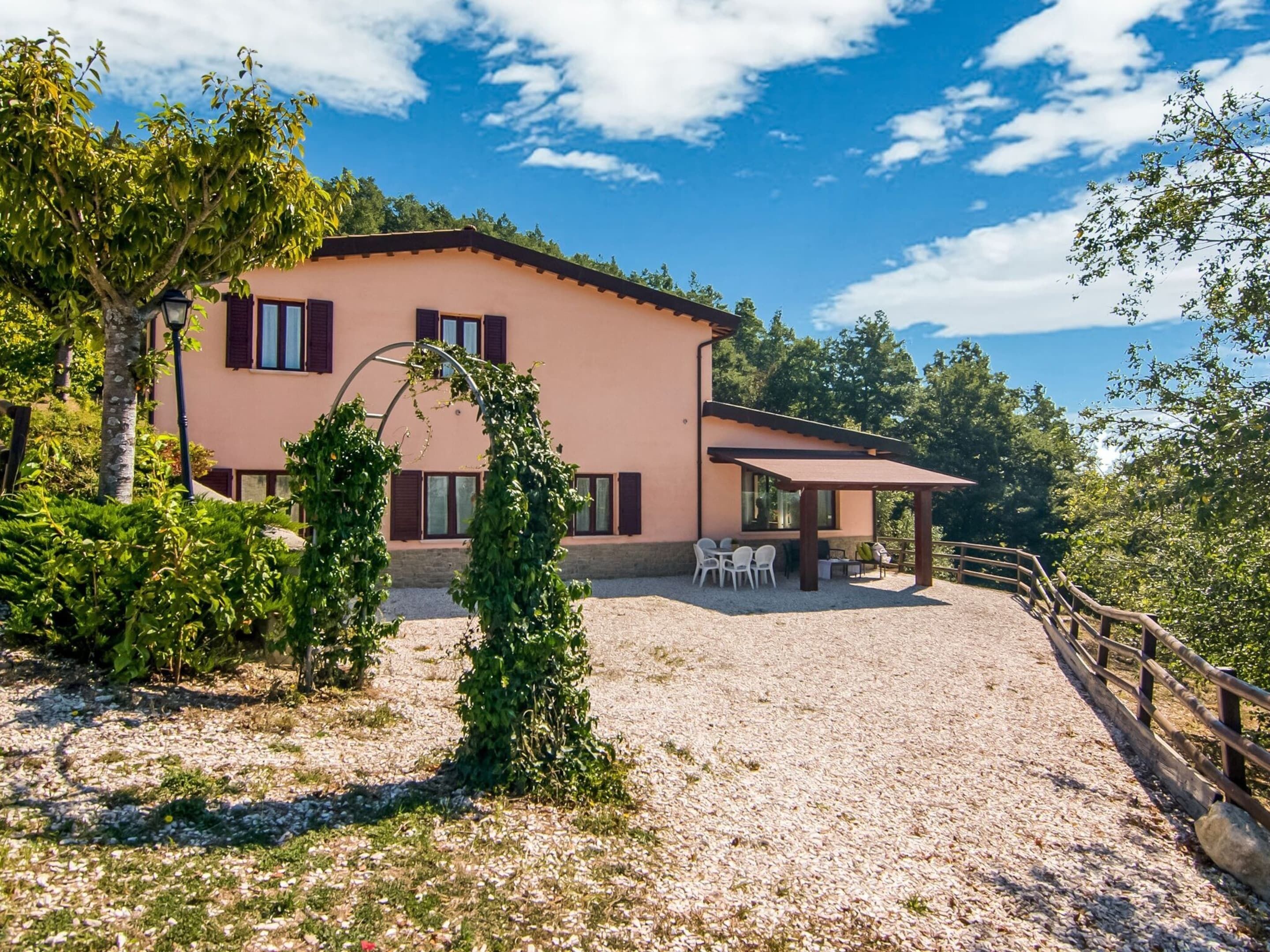 Une maison à deux étages dotée d’un patio, entourée d’arbres et d’un sol en gravier.