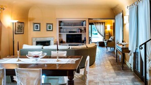 A cozy living room with a fireplace, a dining area with a table set for two, and a bookshelf filled with books. - Belvilla by OYO Villa Arangea Dieci (Marsala)