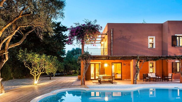 A poolside area with a wooden deck, a pool, and a building with a balcony. - Belvilla by OYO Villa Arangea Dieci (Marsala)