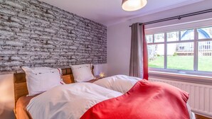 A bedroom with a brick wall, a large window with curtains, and a bed with white and red bedding. - Charming House With Sauna, Jacuzzi in Bullange (Buellingen)