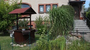 A two-story house with a brick exterior and a red roof. There is a wooden structure with a red roof in the front yard. - Wohnung mit Eigener Terrasse in Wismar (Wismar)
