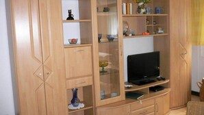 A living room with a wooden cabinet containing shelves, a television, and various decorative items. - Wohnung mit Eigener Terrasse in Wismar (Wismar)