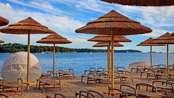 A beachside seating area with thatched umbrellas and wicker chairs, overlooking a calm sea. - Villa in Vabriga With Private Pool & Garden (Tar-Vabriga)
