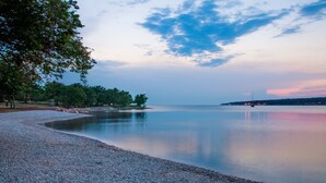 A pebbled beach with calm waters, trees, and a distant shoreline. - Villa in Vabriga With Private Pool & Garden (Tar-Vabriga)