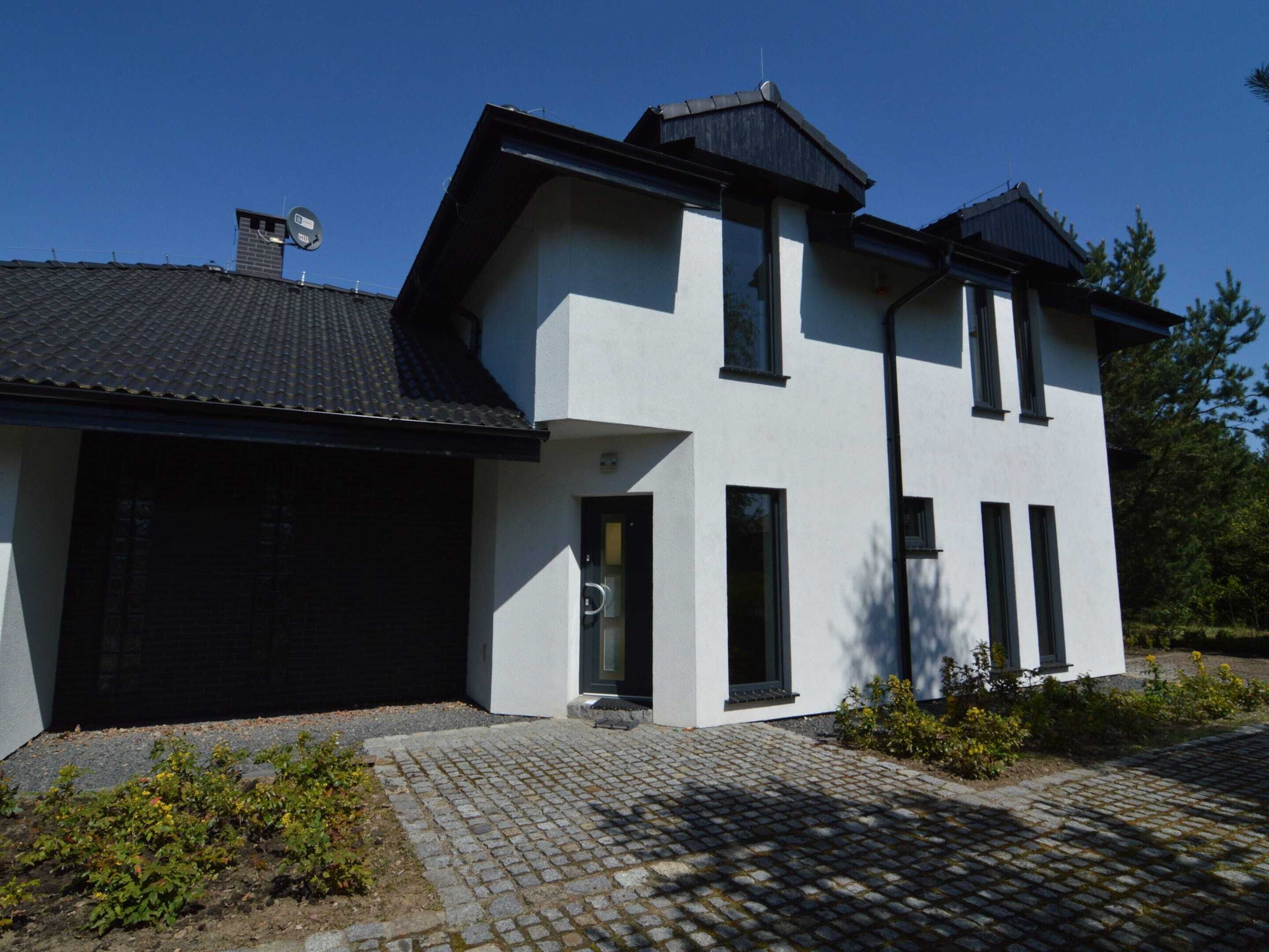 Una casa moderna de dos pisos con techo negro, paredes exteriores blancas y garaje de ladrillo.
