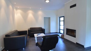 A modern living room with a black leather sofa, a black armchair, and a white coffee table. There is a fireplace on the right wall and a door leading to another room. - Modern Villa With Sauna, Right Next to the Lake (Borne Sulinowo)