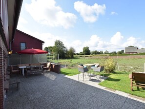 An outdoor patio area with a red umbrella, wooden benches, and a table with chairs. - Charming Apartment in Pugholz Near Sea (Hasselberg)
