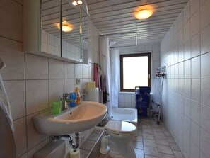 A small, tiled bathroom with a sink, toilet, and a window. - Charming Apartment in Pugholz Near Sea (Hasselberg)