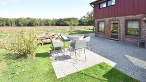 Ein rotes Gebäude mit Backsteinfassade, Außenbereich mit Tischen und Stühlen sowie ein Blick auf ein Feld im Hintergrund.