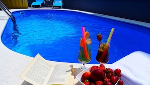 A poolside setting with a book, two drinks, and a bowl of fruit. - Peaceful Villa in Dramalj with Hot Tub (Crikvenica)
