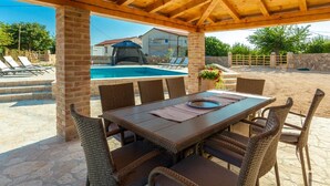 Une terrasse extérieure avec une piscine, des meubles en osier et un espace couvert doté d’un ventilateur de plafond.