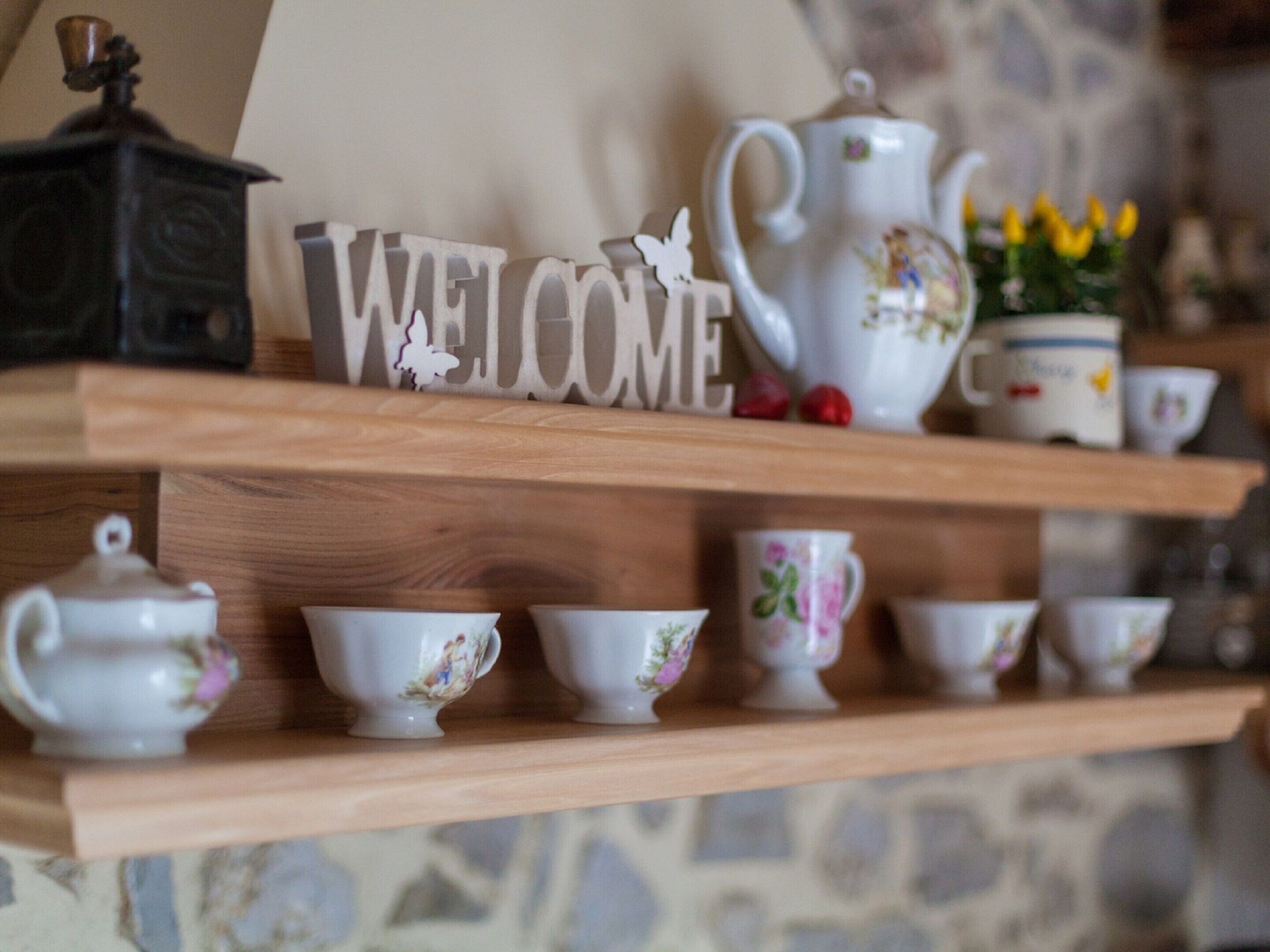 A shelf with a 'WELCOME' sign, teapots, and floral cups.
