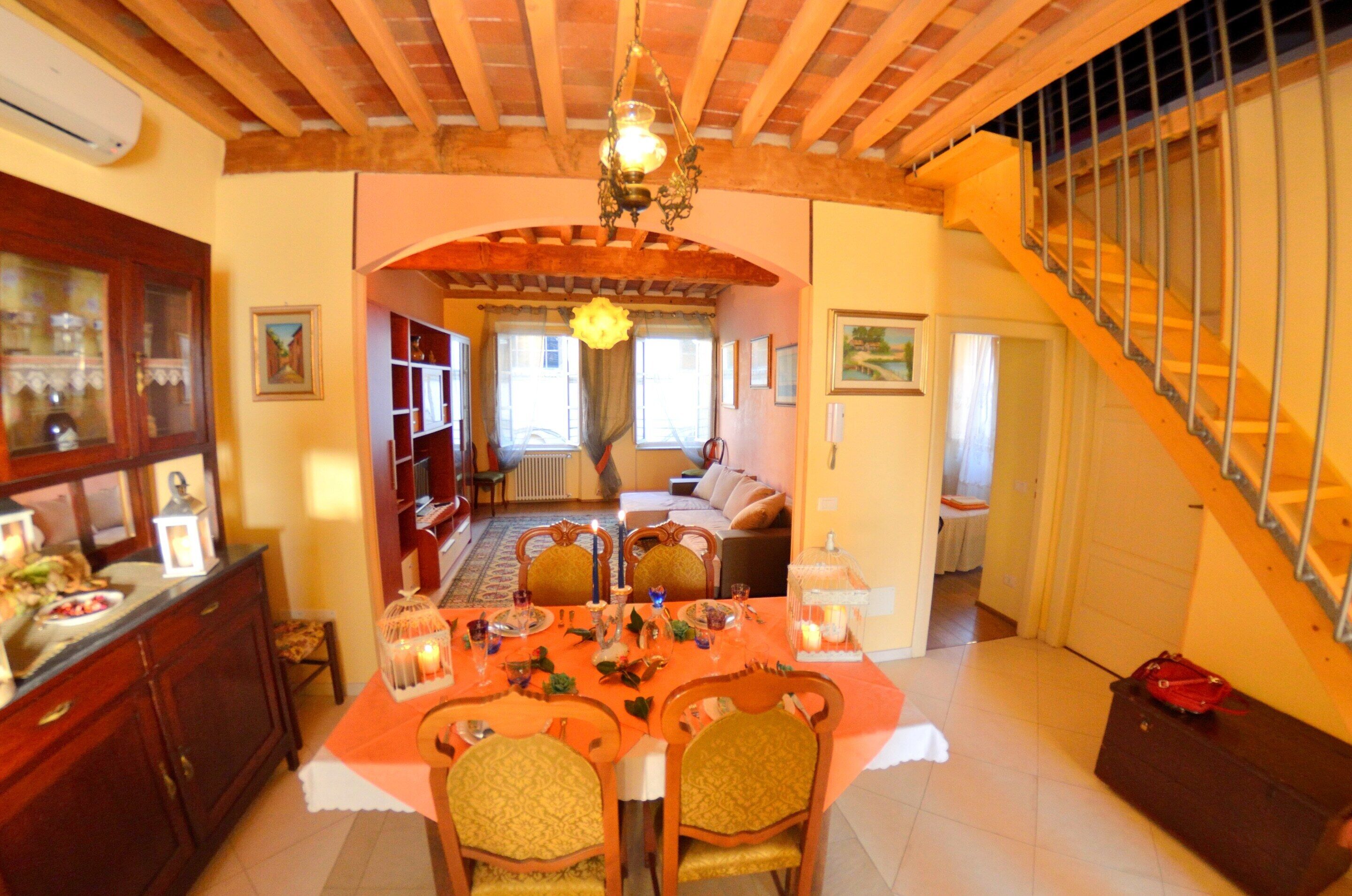 A dining area with a table set for four, a wooden ceiling, and a staircase with a railing.