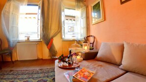 A cozy living room with a sofa, a window with curtains, a radiator, a small table with a tray, a candle, and a framed picture on the wall. - Lucca Retreat With Pool (Lucca)