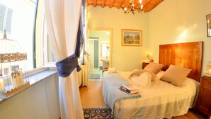 A bedroom with a bed, a window with curtains, a chandelier, a wooden headboard, and a nightstand. - Lucca Retreat With Pool (Lucca)
