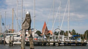 A marina with boats docked, a wooden post in the foreground, and a building with a red roof in the background. - Apartment in Kroepelin Near Baltic Sea (Kroepelin)