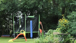 A playground with a slide and a trampoline, surrounded by greenery and a bench. - Apartment in Kroepelin Near Baltic Sea (Kroepelin)