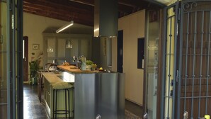 A modern kitchen with a central island, bar stools, and a dining area with a table set for two. - Belvilla by OYO Villa Colle (Recanati)