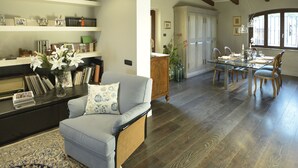 A spacious living room with a sofa, a dining table set for four, and a kitchen area visible through an archway. - Belvilla by OYO Villa Colle (Recanati)