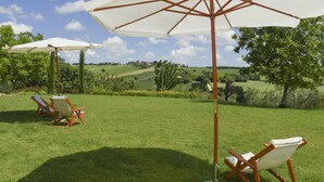 A grassy outdoor area with two wooden chairs and a white umbrella. - Belvilla by OYO Villa Colle (Recanati)