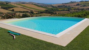 A rectangular swimming pool with a clear blue water, surrounded by a tiled deck and a grassy area. - Belvilla by OYO Mare (Fermo)
