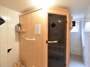 A wooden sauna with a glass door, a small shelf with a container, and a sign on the wall. - Appartement am Meer auf der Insel Poel mit Sauna (Insel Poel)