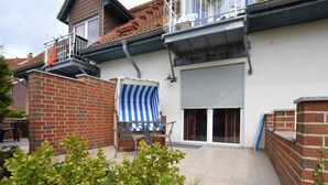 En bostadsbyggnad med en fasad av tegel, en balkong med ett metallräcke, en täckt uteplats med ett randigt solskydd och en skjutdörr av glas.