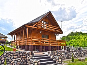A wooden log cabin with a balcony, stone steps, and a stone wall with wheels. - Holiday Home by Lake in Nowa Wioska (Lubrza)